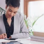 A person writing financial goals in a notebook with coins and a calculator