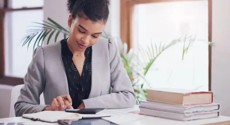 A person writing financial goals in a notebook with coins and a calculator